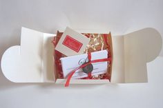 an open gift box with cookies and cards in it on a white tablecloth background