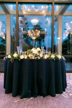 a table with flowers and candles on it in front of a large glass window at night