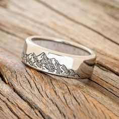 a silver ring with mountains on it sitting on top of a wooden table next to a piece of wood