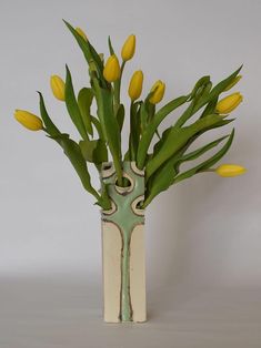 a vase with yellow flowers in it sitting on a table next to a white wall