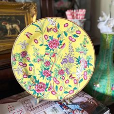 a yellow plate sitting on top of a stack of magazines next to a vase with flowers