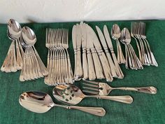 an assortment of silverware including spoons, forks and knives on a green cloth