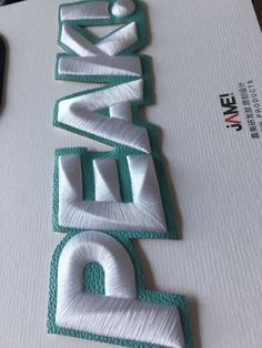 the letters are made out of white and green thread on top of a piece of paper