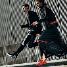 two people in black and red outfits are walking down the street with one person on a scooter