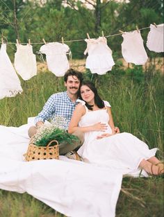 a man and woman sitting next to each other on top of a blanket in the grass