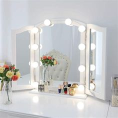 a white vanity mirror with lights on it and flowers in vase next to the mirror