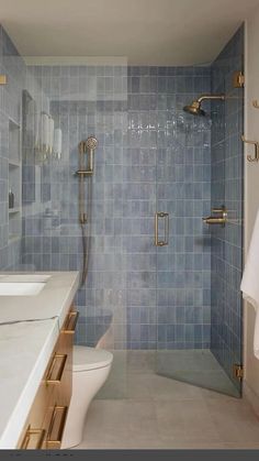 a blue tiled bathroom with two sinks and a walk in shower next to a toilet