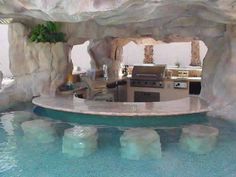 an outdoor kitchen and grill area in a pool that looks like a cave with rocks on the sides