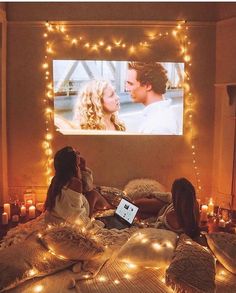 two people sitting on a bed watching a movie in front of a screen with candles