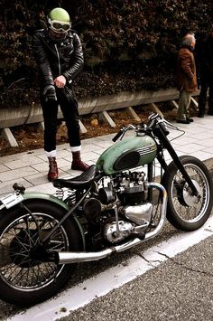 an old motorcycle is parked on the side of the road with someone standing next to it