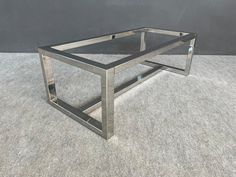 a metal and glass coffee table on carpeted floor with grey wall in background,