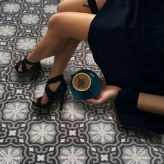 a woman is sitting on the floor with her feet up and holding a coffee cup