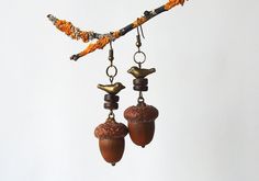 two acorns hanging from a tree branch with beads and bird charms on them