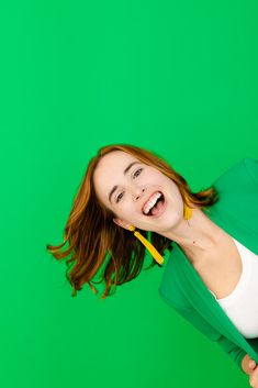 a woman is smiling and holding a toothbrush in her mouth while standing against a green background