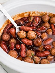 a spoon full of meatballs and beans in a white crock pot on a table