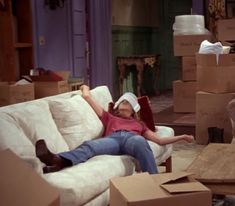 a woman laying on top of a couch in a living room filled with cardboard boxes