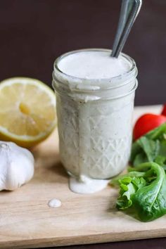 a glass jar filled with white sauce next to some vegetables and lemons on a cutting board