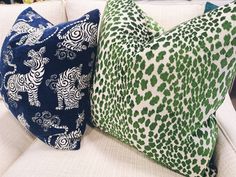 two pillows sitting on top of a couch in front of a white sofa with green and blue patterns