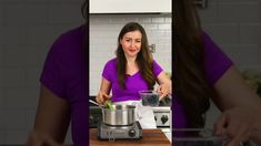 a woman standing in front of a pan on top of a counter next to a blender