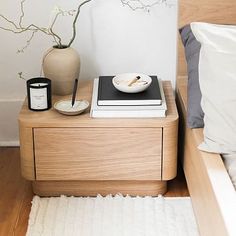 a nightstand with a book, bowl and candle on it next to a white rug