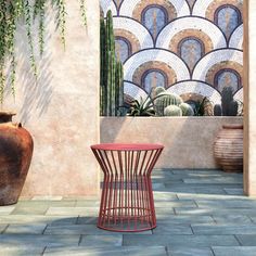 a red table sitting on top of a stone floor next to a potted plant