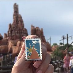 a person holding up a small stamp with a castle in the background