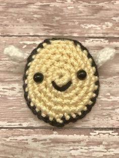 a crocheted smiley face with two black eyes on a white wooden background,