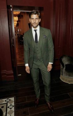 a man in a green suit and tie standing next to a door with his hands in his pockets