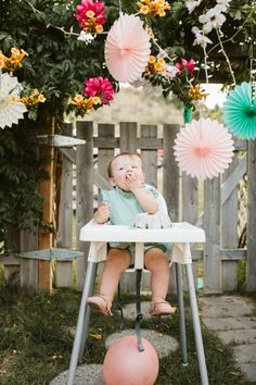 a baby sitting in a highchair eating food with paper flowers hanging from the ceiling