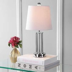 a glass table with a lamp on top and a book sitting next to it in front of a mirror