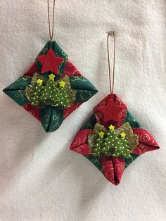 two origami christmas ornaments hanging on a white towel with red and green decorations