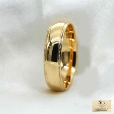 a gold wedding ring with an engraved design on the outside and inside, sitting on a white background