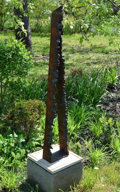 a metal sculpture in the middle of a grassy area with trees and bushes behind it