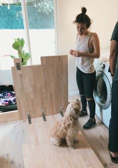 a woman standing in front of a dryer next to a dog on the floor