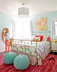 a girl standing next to a bed in a room with pink and green decor on the walls