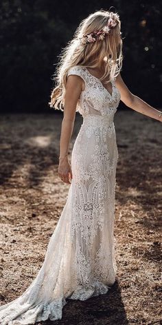 a woman in a white wedding dress holding her hand out to the side with trees in the background