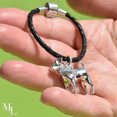 a hand holding a silver cow charm on a black leather cord bracelet with an adjustable clasp