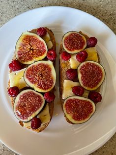 a white plate topped with two pieces of toast covered in cheese and figs next to raspberries