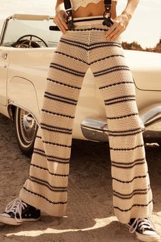 a woman standing in front of a car wearing high waisted pants and crop top