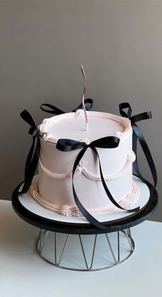 a white cake sitting on top of a metal stand with black ribbon around the edges