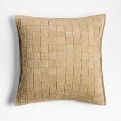 a tan pillow with woven squares on the front and back, sitting against a white wall