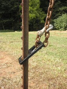 a chain link is attached to a metal pole in the grass with trees in the background