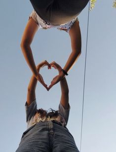 two people making a heart shape with their hands while standing on top of each other