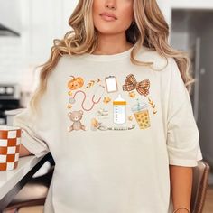 a woman standing in front of a counter wearing a white shirt with various items on it