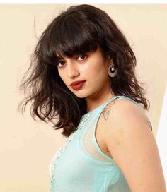 a woman with long dark hair wearing a blue top and red lipstick is posing for the camera