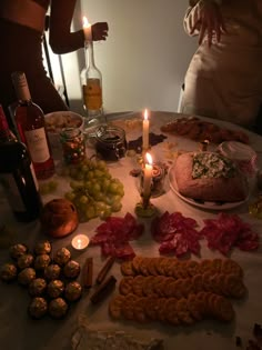 a table topped with lots of food next to candles and wine bottles on top of it