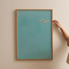 a person is holding up a painting with two birds flying in the sky on it