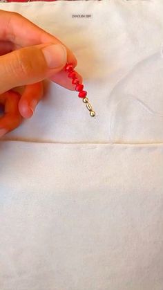 someone is stitching the beading on a white piece of fabric with red beads