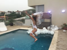 a woman jumping into a swimming pool with her arms in the air while wearing a white bodysuit