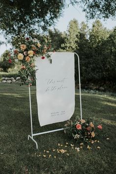 a sign that is sitting in the grass with flowers on it and some leaves around it